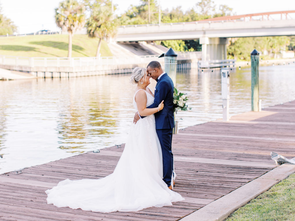 Bride and groom touch foreheads in front of waterfront bridge at their Channel Side Wedding in Palm Coast, Florida. Taken by Ashley Dye Photography, a Jacksonville, Florida Wedding Photographer.