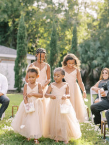 Four flower girls in pink dresses coming down the aisle at a Channel Side Wedding in Palm Coast, Florida. Taken by Ashley Dye Photography, a Jacksonville, Florida Wedding Photographer.