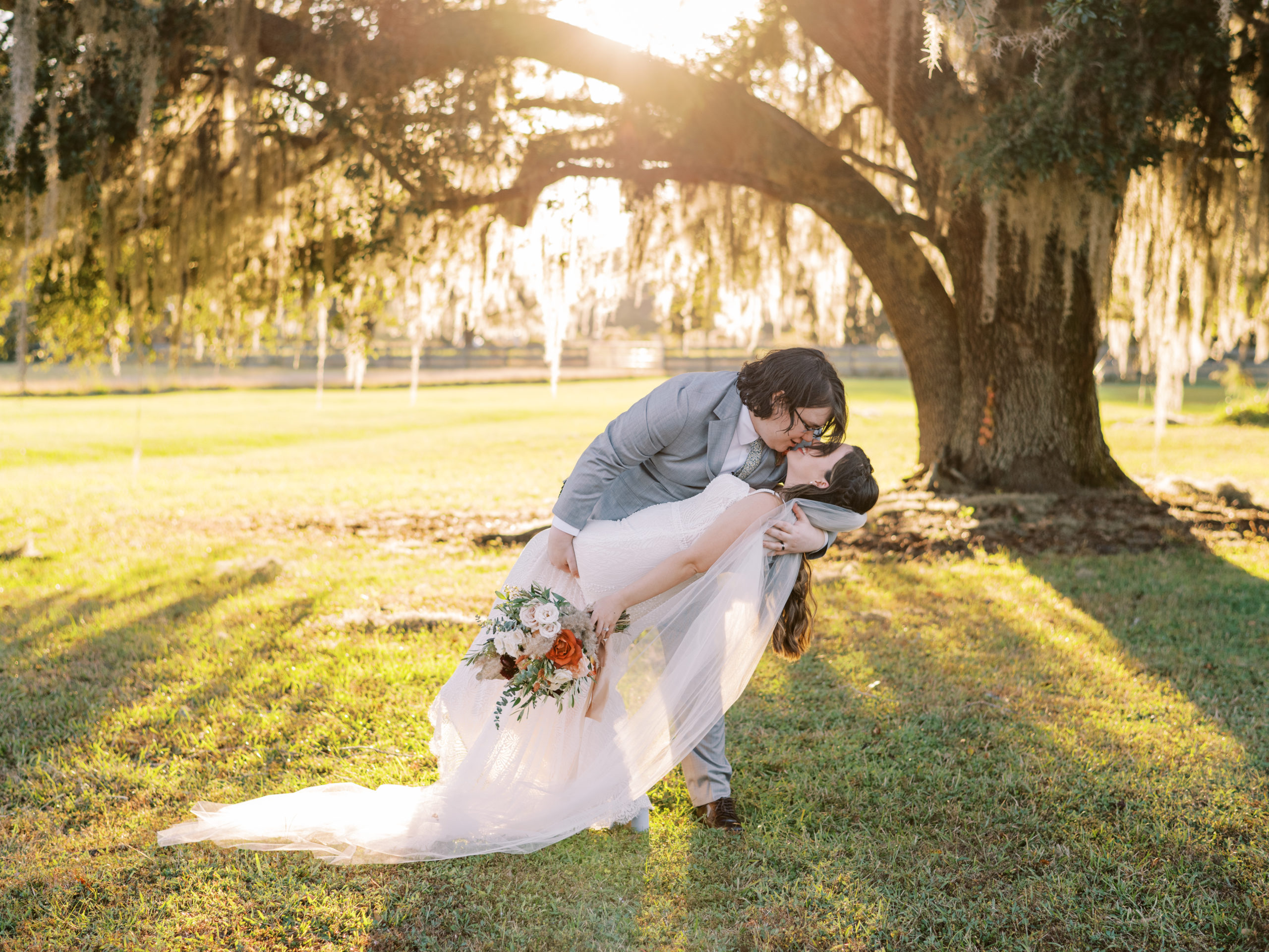 Bride and groom kiss under tree with sunlight coming through at their Belle Oaks Barn Wedding captured by Ashley Dye Photography, a St. Augustine, Florida wedding photographer.